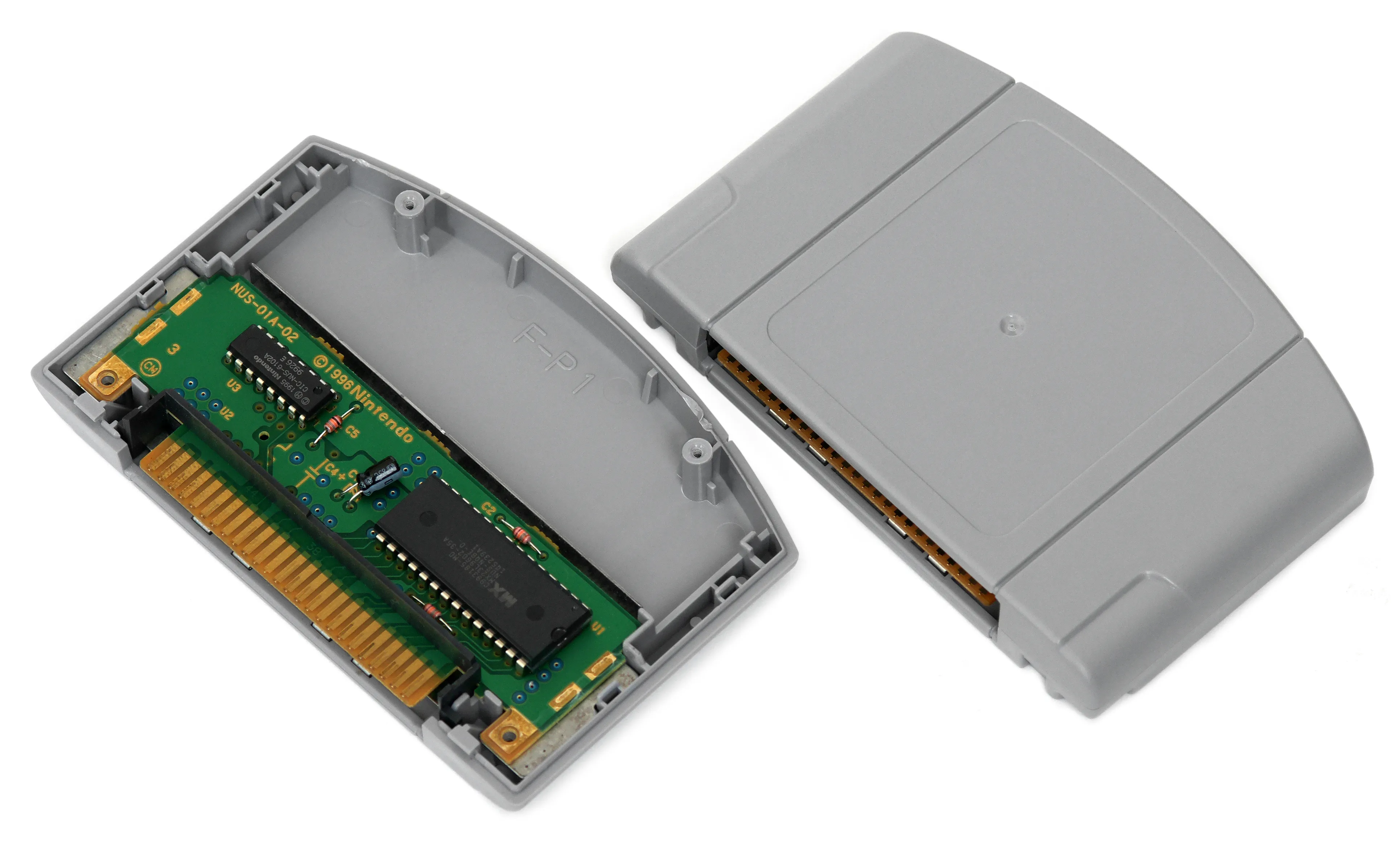 A grey Nintendo 64 game cartridge opened up to show its green circuit board, next to a closed cartridge